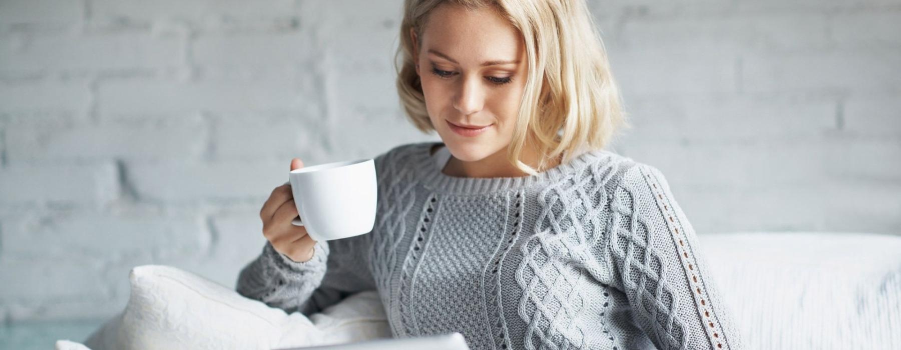 a woman sits on a couch with a cup of coffee and looks at her tablet